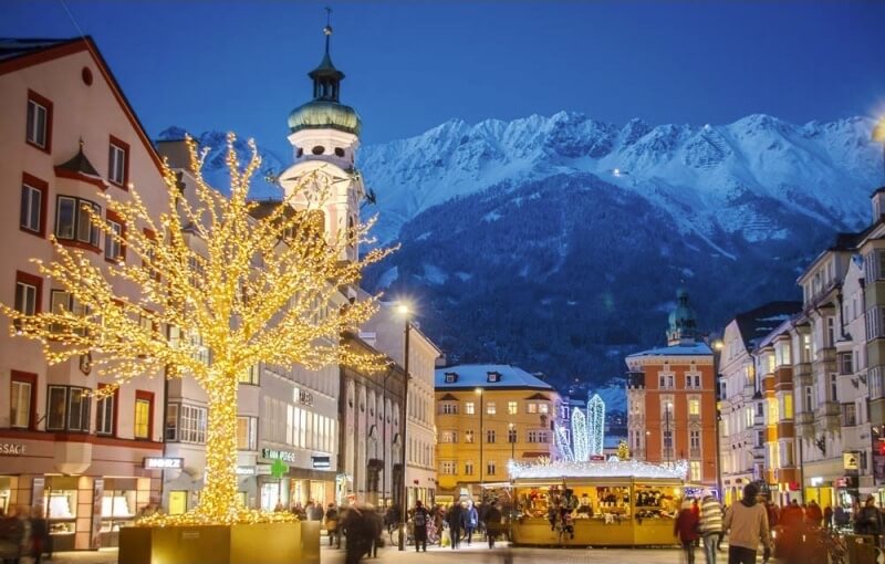 Bild av en promenad i Innsbruck, med ljustäckta träd och de mäktiga alperna i bakgrunden